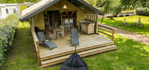 Safaritent lodge op Camping Kost Ar Moor in Frankrijk, met houten terras en kinderen die fietsen.
