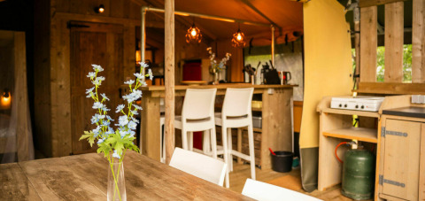 Interior de una tienda Safari lodge en Camping Kost Ar Moor, Francia, con muebles rústicos de madera y flores.