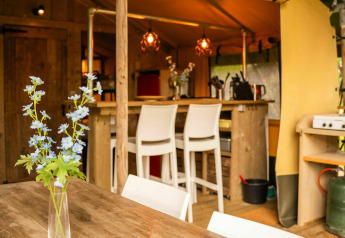 Interior de una tienda Safari lodge en Camping Kost Ar Moor, Francia, con muebles rústicos de madera y flores.