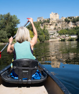 Mujer navegando en canoa por un río cerca de Marcillac St. Quentin, con un castillo visible en la colina.