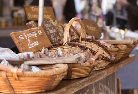 Puesto de mercado francés con cestas de embutidos y carteles escritos a mano cerca de Marcillac St. Quentin.