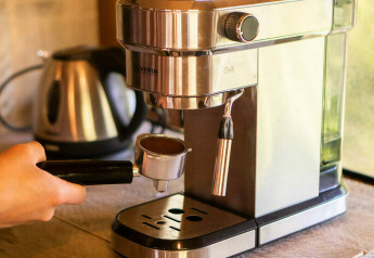 Una mano tiene un portafiltro a una macchina da espresso in una tenda safari al Camping Les Tailladis, Francia.