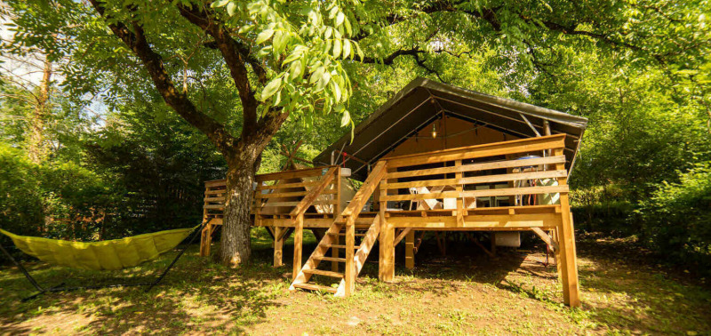 Safari Lodge + Teeny Lodge : Tente safari sur plateforme en bois avec hamac sous arbres, nature verdoyante paisible.