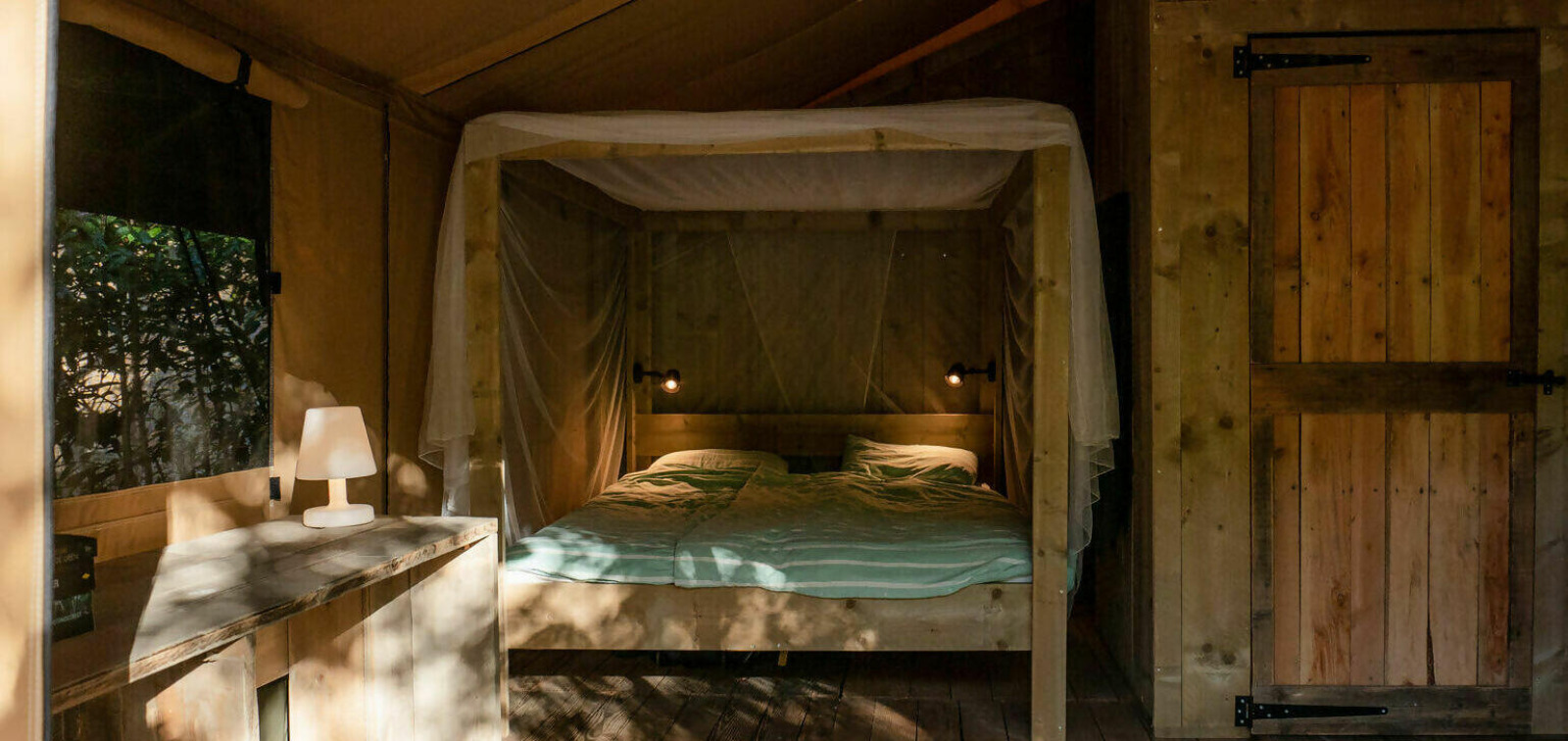 Interieur van de Safari Lodge met tweepersoonsbed, nachtlampje en houten meubels bij Camping Les Tailladis.