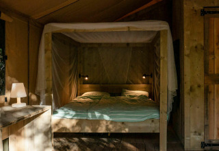 Vista interior de Safari Lodge con cama doble, lámpara de mesa y muebles de madera en Camping Les Tailladis.