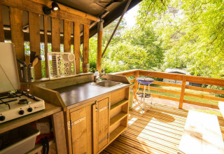 Outdoor kitchen with a gas stove, sink, and wooden deck surrounded by lush greenery in a safari tent.