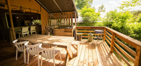 Terraza exterior del Safari Lodge en Camping Les Tailladis, Francia, con mesa de comedor y barbacoa.