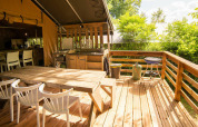 Terraza exterior del Safari Lodge en Camping Les Tailladis, Francia, con mesa de comedor y barbacoa.