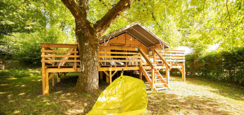 Tienda elevada de madera bajo árboles en Camping Les Tailladis, Nouvelle-Aquitaine, Francia, en verano.