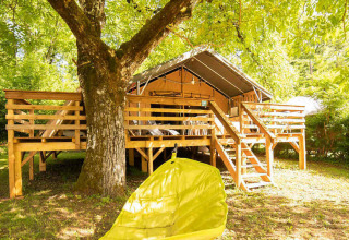 Tenda su terrazza di legno sotto alberi a Camping Les Tailladis, Nouvelle-Aquitaine, Francia, in estate.