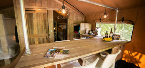 Vista interior de la tienda Safari Lodge en Camping Les Tailladis, Francia, con muebles rústicos de madera.