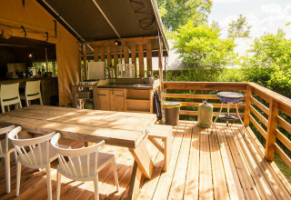 Holzterrasse am Safari Lodge Zelt auf Camping Les Tailladis in Frankreich, mit Esstisch und Grill.