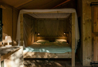 Indvendigt billede af Safari Lodge telt ved Camping Les Tailladis, Frankrig, med træmøbler og seng.