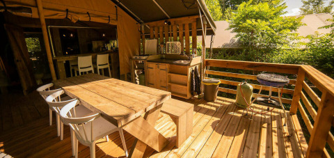 Terraza exterior en Safari Lodge en Camping Les Tailladis, Francia, con mesa y sillas de madera.