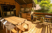 Terraza exterior en Safari Lodge en Camping Les Tailladis, Francia, con mesa y sillas de madera.