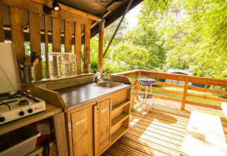 Cocina y comedor al aire libre de una tienda safari en Camping Les Tailladis, Francia, rodeados de árboles.