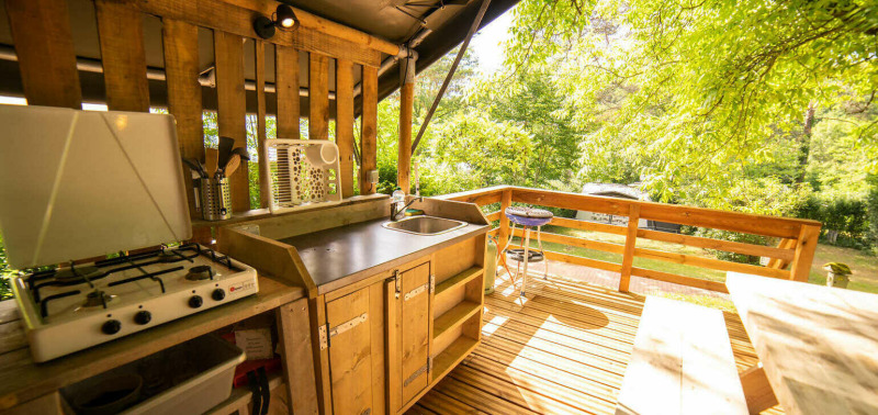 Cocina y comedor al aire libre de una tienda safari en Camping Les Tailladis, Francia, rodeados de árboles.