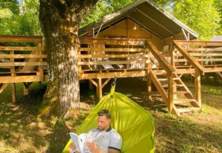 Uomo che legge su un'amaca sotto un albero davanti a una baita a Camping Les Tailladis, Nouvelle-Aquitaine.