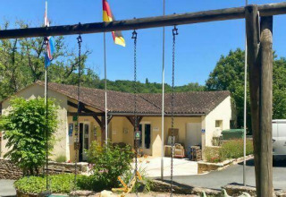Photo of Camping Les Tailladis featuring swings, the main building, flags, and a white van in the background.