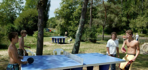 Niños juegan al tenis de mesa al aire libre en Camping Les Tailladis, rodeados de naturaleza en Francia.