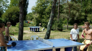 Niños juegan al tenis de mesa al aire libre en Camping Les Tailladis, rodeados de naturaleza en Francia.