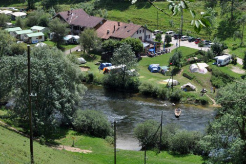 Parque vacacional con glamping, tiendas, caravanas y personas remando en el río junto a zonas verdes.