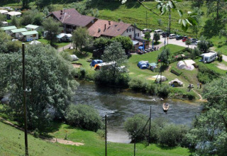 Parco vacanze con tende glamping, roulotte e persone in canoa su un fiume in ambiente verde.