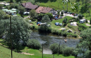 Parco vacanze con tende glamping, roulotte e persone in canoa su un fiume in ambiente verde.