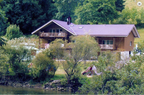 Parque vacacional con una gran cabaña de madera junto al río, ideal para alojamiento de glamping.