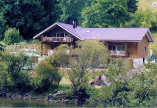 Vakantiepark met grote houten lodge aan een rivier, omringd door natuur, perfect voor glampingverblijven.