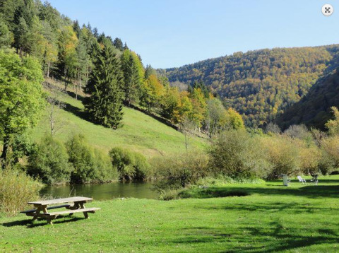 Udsigt over frodig dal med picnicbord, græsplæne, en flod og træbeklædte bakker i et feriepark.
