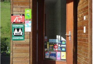 Ingang van een vakantiepark met glamping, houten gevel, deur vol stickers en bloempot.