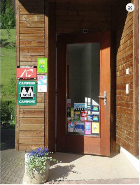 Entrée d’un parc de vacances glamping, façade en bois, porte couverte d’autocollants et pot de fleurs.