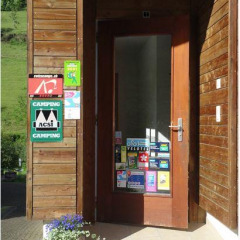 Entrée d’un parc de vacances glamping, façade en bois, porte couverte d’autocollants et pot de fleurs.