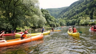 Folk nyder kanotur på en flod omgivet af skove ved en feriepark med glamping i naturskønne omgivelser.