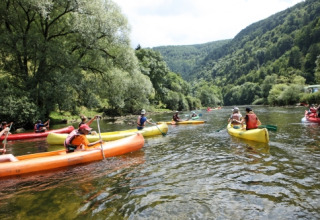 Personas navegando en kayak por un río en un parque vacacional con glamping, rodeados de bosques verdes.
