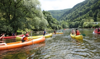 Folk nyder kanotur på en flod omgivet af skove ved en feriepark med glamping i naturskønne omgivelser.