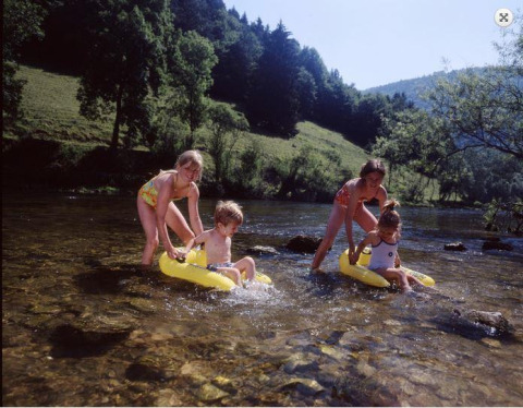 Kinderen spelen op opblaasbootjes in een ondiepe rivier bij een vakantiepark met glampingverblijf.