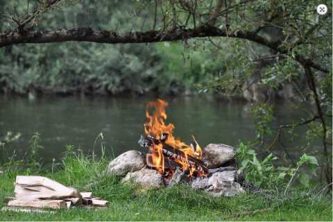 Kampvuur aan het water, omringd door groene natuur, voor gezellige avonden bij het glampen.