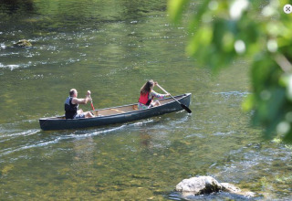 Dos personas reman en una canoa por un río tranquilo en un parque vacacional con glamping entre la naturaleza.