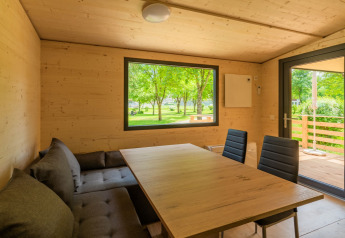 Eethoek in een houten lodge bij Drau Camping Sachsenburg, Oostenrijk, met uitzicht op groene bomen buiten.