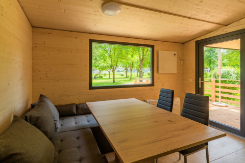 Eethoek in een houten lodge bij Drau Camping Sachsenburg in Oostenrijk, met zicht op groene bomen buiten.