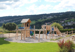 Wooden playground at Camping Lac des Brenets, a holiday park in Neuchâtel, Switzerland, with hills in background.