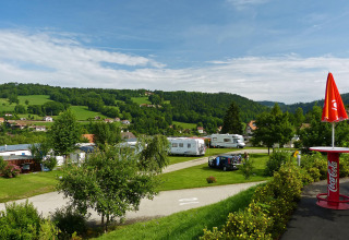 Camping Lac des Brenets in Neuchâtel, Zwitserland met caravans, groene weiden en blauwe lucht op de achtergrond.