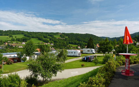 Camping Lac des Brenets en Neuchâtel, Suiza, con autocaravanas, verdes prados y colinas bajo un cielo azul claro.