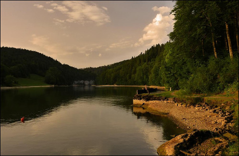 View of Camping Lac des Brenets, a peaceful lake and forest setting in Neuchâtel, Switzerland at sunset.