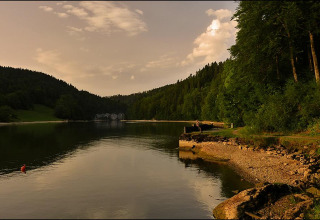 View of Camping Lac des Brenets, a peaceful lake and forest setting in Neuchâtel, Switzerland at sunset.