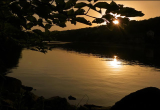 Sunset over the lake at Camping Lac des Brenets in Neuchâtel, Switzerland, seen through leafy branches.