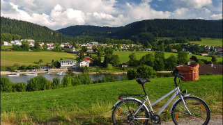 Vista de pueblo, lago, barcos y colinas cerca de Camping Lac des Brenets, Neuchâtel, Suiza, bicicleta en primer plano.