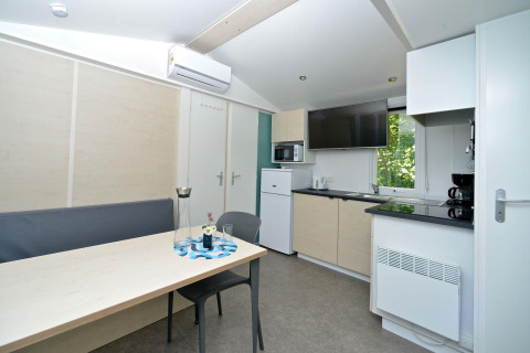 Modern mobile home kitchen and dining area at Drau Camping Sachsenburg, Austria, featuring TV and aircon.